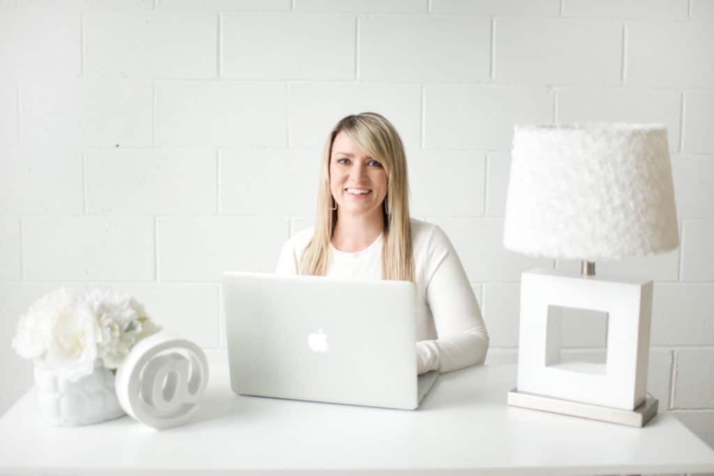 A person sits at a table with a laptop and a white wall.