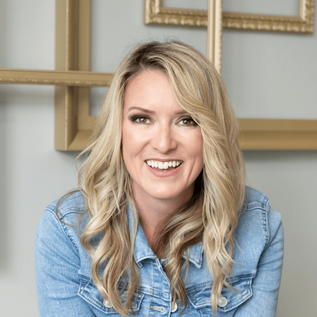 A smiling person with long blond hair and a denim jacket sits in front of a neutral background with decorative golden frames. They seem joyful and relaxed.
