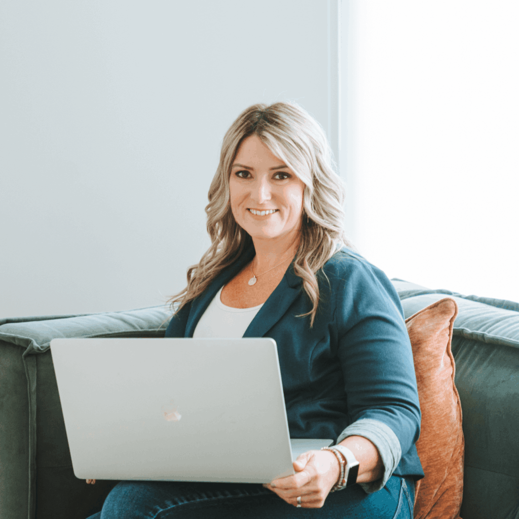 A person sits on a couch with a laptop, smiling. The setting is bright and modern with a minimalist style.