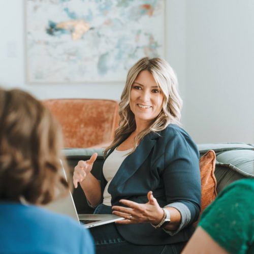 Three people are engaged in a discussion around a laptop in a bright, modern room with abstract art on the wall.