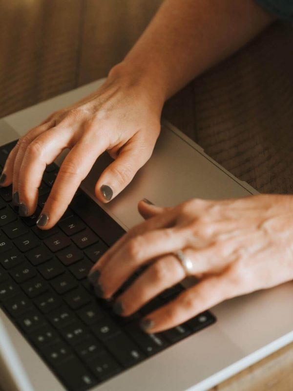 A person typing on a laptop wearing a smartwatch with a blue band, positioned on a wooden surface.
