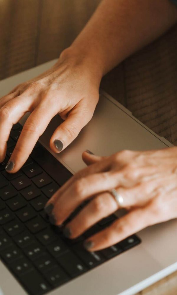 A person typing on a laptop wearing a smartwatch with a blue band, positioned on a wooden surface.