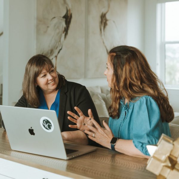 Two people talking at a table with a laptop. Artwork depicting birds is in the background, creating a cozy, conversational setting.