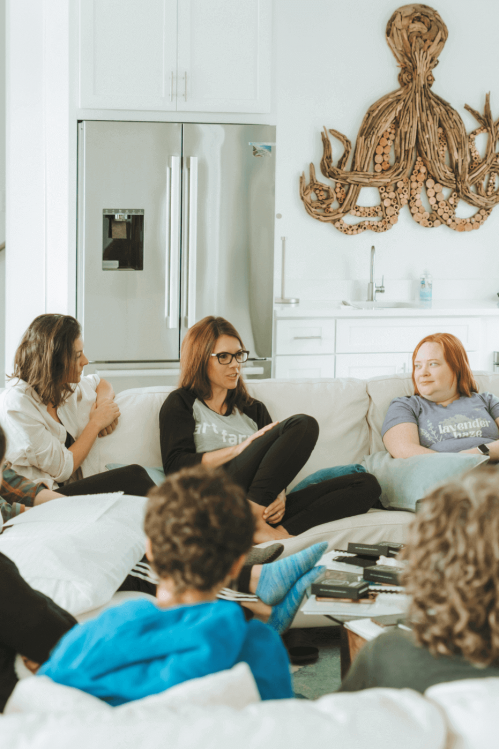 A group of people are sitting on a sofa, engaged in conversation. A wooden octopus decoration is mounted on the wall.