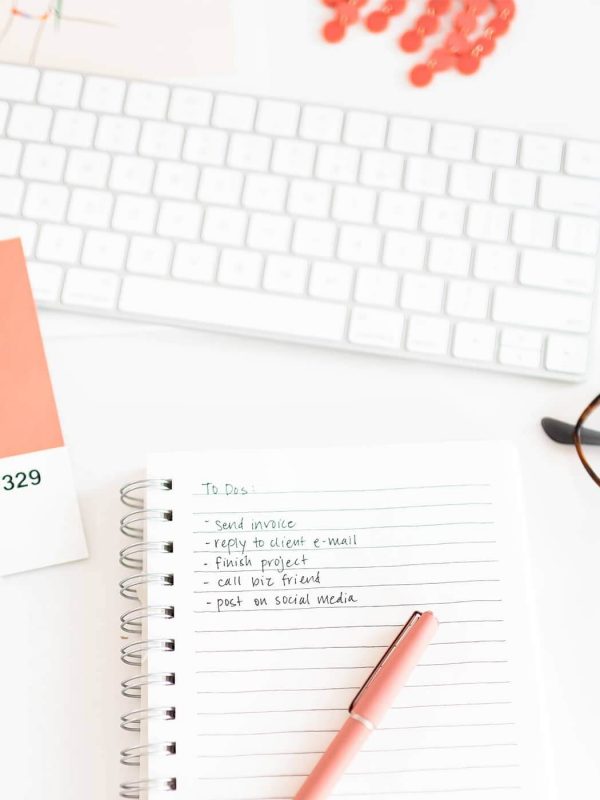 Workspace includes a keyboard, notebook with a to-do list, glasses, color swatch, and pen. Items organized neatly on a white surface.