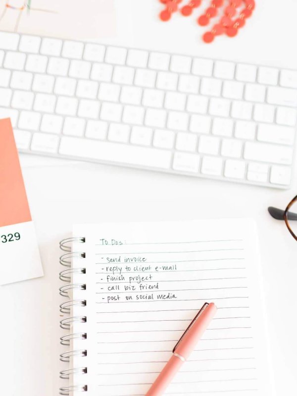 Desk setup with a keyboard, pink pen, glasses, and notepad listing tasks. Coral design swatches add a pop of color.